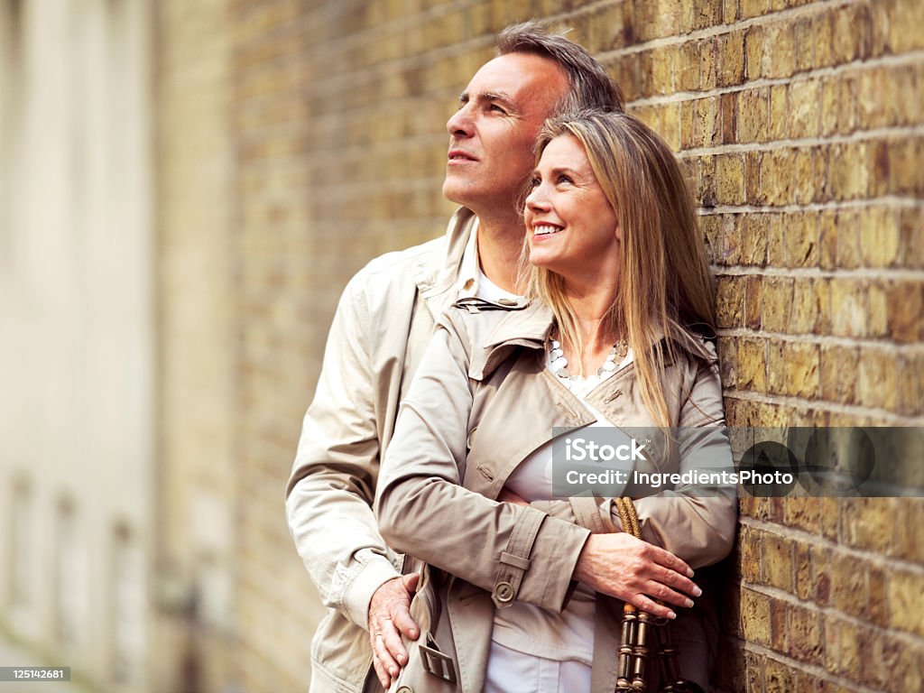 Sorrindo casal abraçando e em pé ao lado da parede de tijolos. - Foto de stock de 50 Anos royalty-free