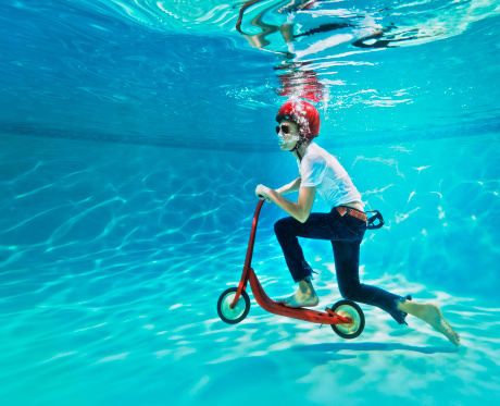 teenager riding a push scooter underwater, on a swimming pool.