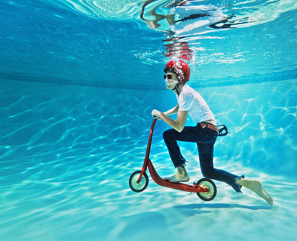 teenager pushing a scooter underwater teenager riding a push scooter underwater, on a swimming pool. Bizarre stock pictures, royalty-free photos & images