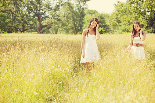 Two little girls, sisters in white dresses picking flowers in the nature