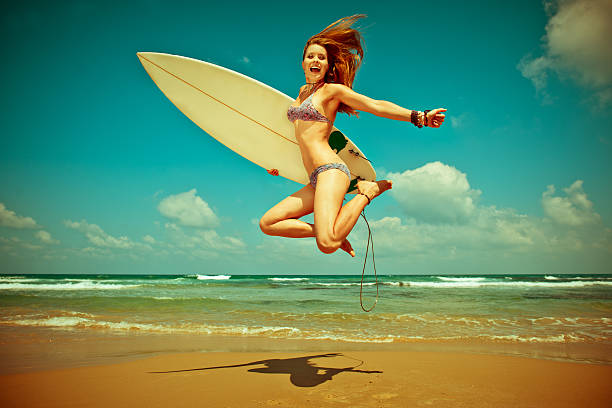 Young beautiful woman happly jumping with surf-board on the beach, surfing lifestyle