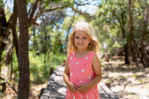 A front-view shot of a young girl wearing a pink sundress, she is smiling and looking at the camera on a sunny day in Perth, Australia.