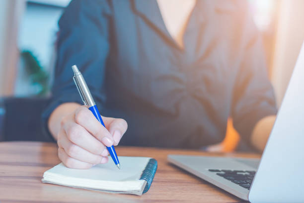 istock Woman is writing on a notebook with a pen and using a laptop to work in the office. 1251436795