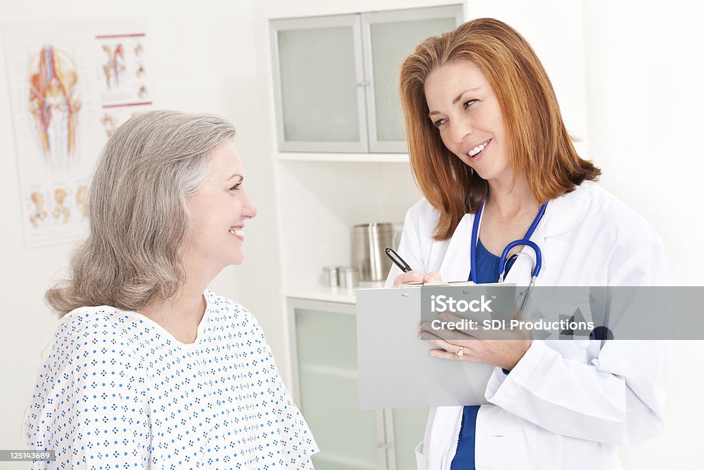 Uśmiechający się lekarz notatek i komunikowania się z szczęśliwy pacjenta - Zbiór zdjęć royalty-free (Aktywni seniorzy)