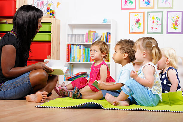 lehrer/pflegekraft/kindermädchen lesung zu einer gruppe von kinder im kinderzimmer - preschooler stock-fotos und bilder