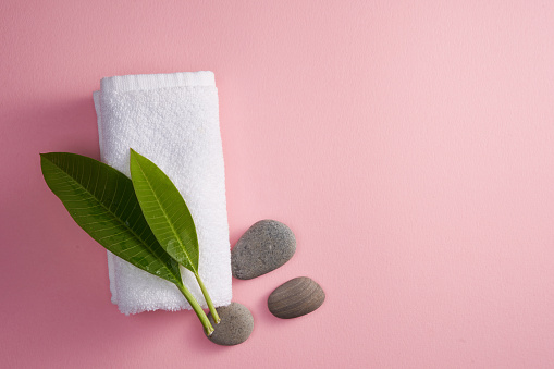 beach pebbles and towel with fragipani leaf on pink background