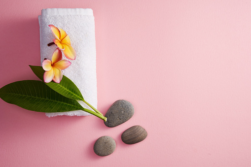 frangipani flowers, beach pebbles and towel on pink background