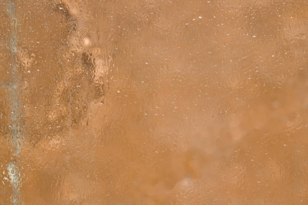 istock Texture. A fragment of a glass surface covered with a thin layer of melting ice is located on a light brown background. Close-up. 1251440459