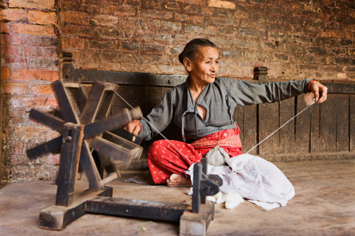 Smiling woman carding raw wool with old vintage wooden machine in cozy rustic house in countryside