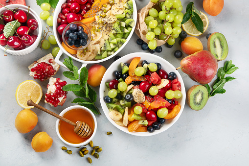 Bowl of healthy fresh fruit salad on grey background. Top view, flat lay with copy space