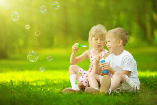 Happy cute friends playing with soap bubble in a field.