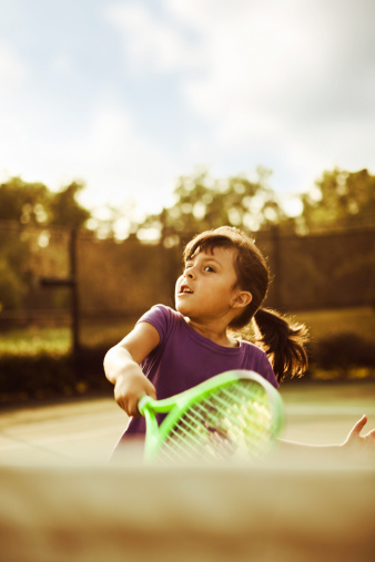 Little girl playing tennis, swings with force.