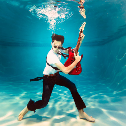 teenager playing an electric guitar underwater on a swimming pool.