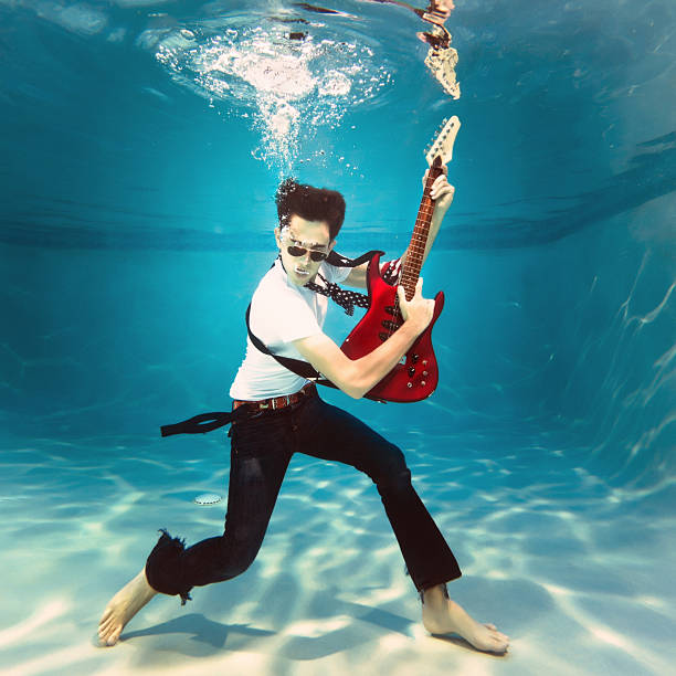 underwater rock and roll teenager playing an electric guitar underwater on a swimming pool. rock musician photos stock pictures, royalty-free photos & images