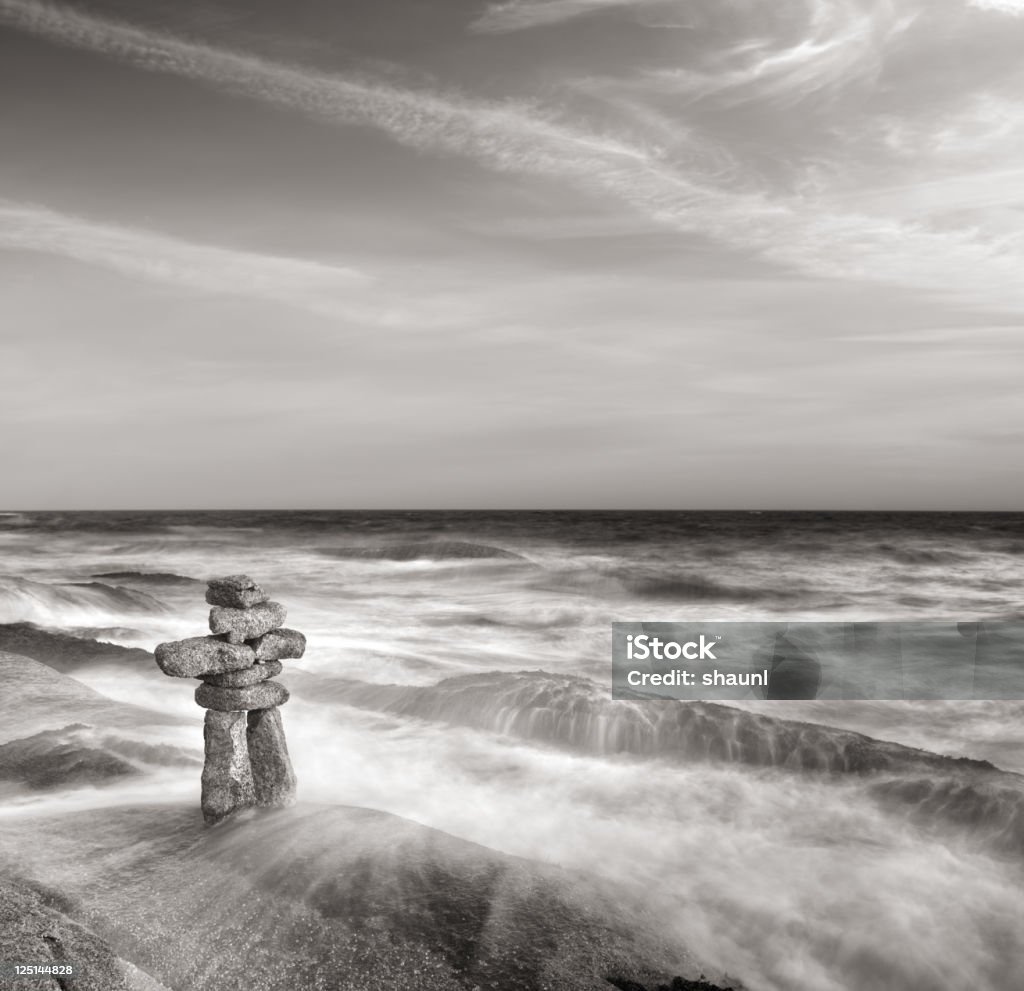 Inuksuk An inuksuk stands defiantly in the surf.  Long exposure, toned black & white. Atlantic Ocean Stock Photo
