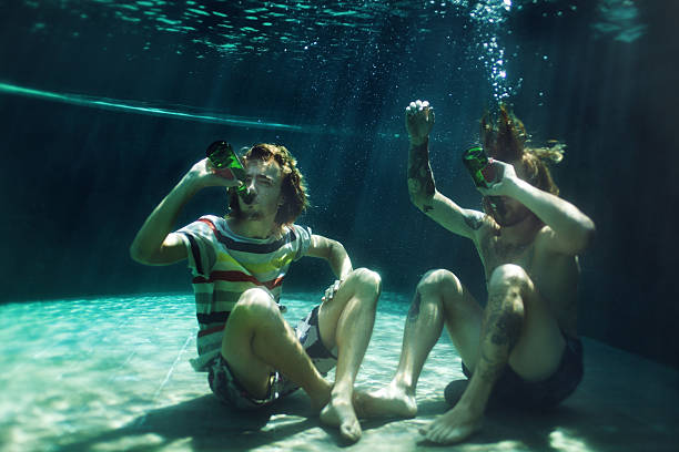 deux jeunes hommes de boire de la bière à la piscine - water touching sensory perception using senses photos et images de collection
