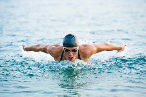 Front view of young female professional swimmer at butterfly stroke; practicing in the sea