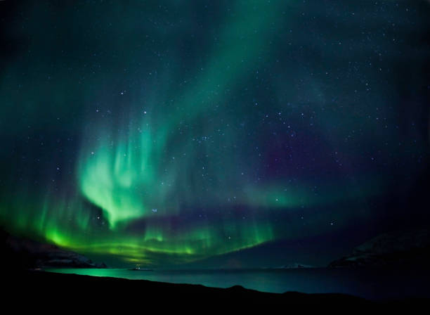 The northern lights aurora borealis in blue and green Aurora borealis above a fjord near Tromso in Norway.  Some noise due to long exposure. aurora polaris stock pictures, royalty-free photos & images