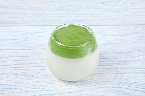 Dalgona matcha latte in a glass cup on a wooden background.