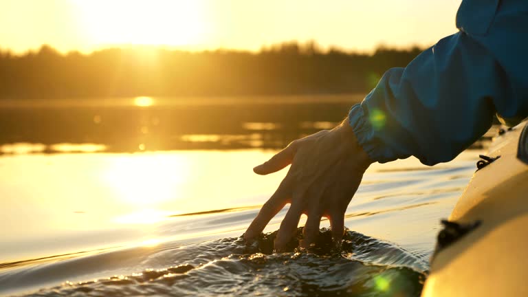 man puts fingers down lake kayaking against backdrop of golden sunset, unity harmony nature