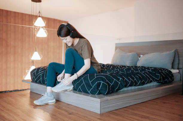 アジアの中国の女性は彼女の靴を履いて彼女の寝室で彼女のアパートから出て行く準備をしている服を着ています - foundation bed ストックフォトと画像
