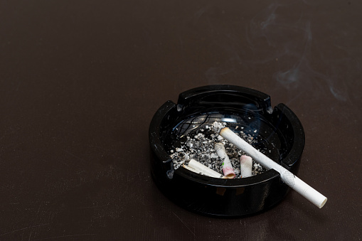 Smoking is bad for your health. Black ashtray with cigarette butts. Smoked cigarette with smoke