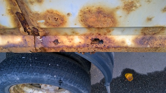 Sheet metal corrosion of old vehicle steel. Rusty surface, background. Damaged texture. Protection and painting auto in winter. Professional paintwork. Car bodywork concept. Truck parts and wheel.