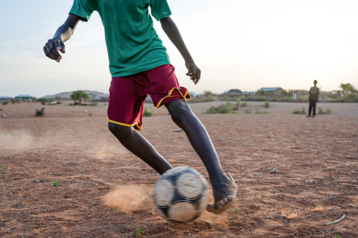 Melkadida, Ethiopia - 11/24/2018: African boy plays football with his bare foot in Somali refugee camp Melkadida, Dollo Ado, Ethiopia