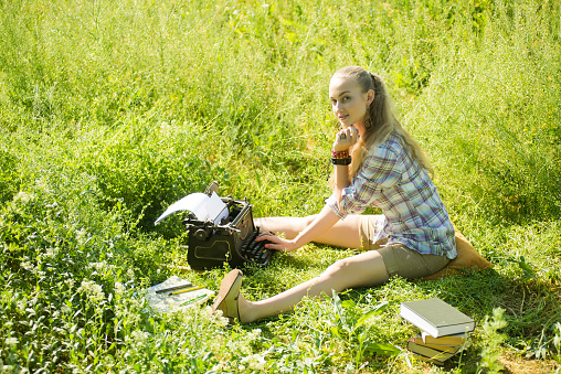 beautiful young blonde hair woman types on vintage typewriter at outdoor