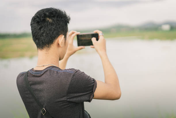 istock Young Asian man standing looking at the view and taking photo 1251479224