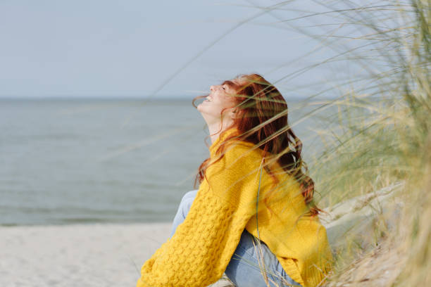 Happy young woman giggling to herself Happy young woman giggling to herself as she relaxes on sandy beach in autumn enjoying the warmth of the sun baltic sea stock pictures, royalty-free photos & images