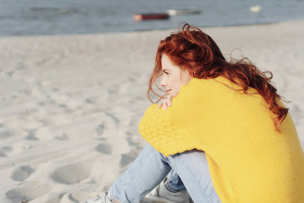 istock Lonely young woman sitting alone on a sandy beach 1251480906