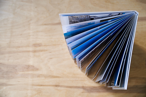 Close-up picture of firm photo book pages on wooden table. Flat lay picture of travel printed album. Photography package. Family memories in pictures.