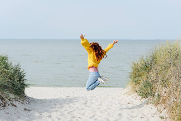 해변에서 기쁨을 위해 노란색 점프에 소녀 - beach women joy sand 뉴스 사진 이미지