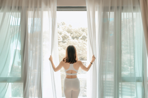 an asian chinese beautiful woman opening curtain and walking out to the balcony in the morning getting ready to practice yoga