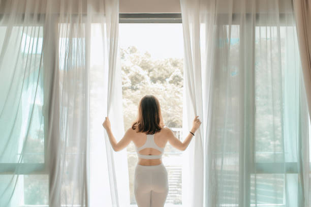 an asian chinese beautiful woman opening curtain and walking out to the balcony in the morning getting ready to practice yoga - door curtain imagens e fotografias de stock
