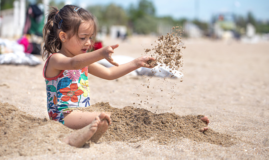 Little girl playing with sand on the beach. A cheerful child. The concept of summer vacation.