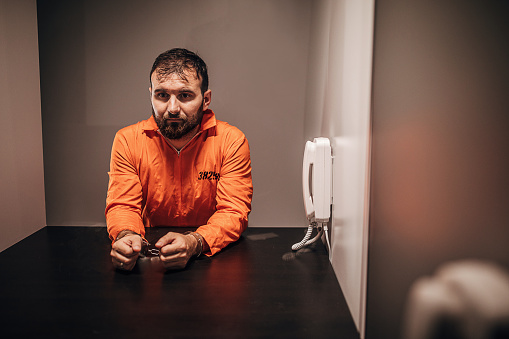 One male prisoner in orange jumpsuit having a visit in prison visiting room.