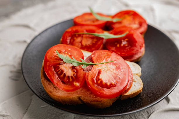 istock Three sandwiches with fresh and bright red tomatoes and smoked sausage, decorated with a leaf of green arugula on a matte black plate 1251497939