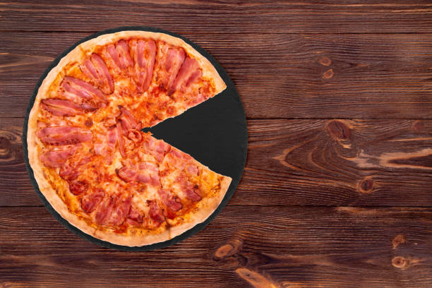 istock Pizza becon, without slice, on slate bottom, on wooden table 1251502368