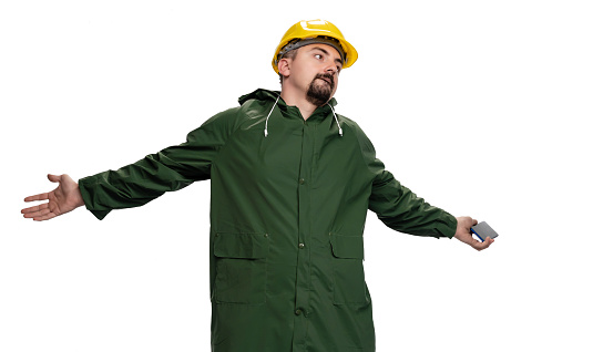 Angry engineer with green raincoat and hardhat using smartphone on white background. Photo is taken in studio environment with Sony A7III camera