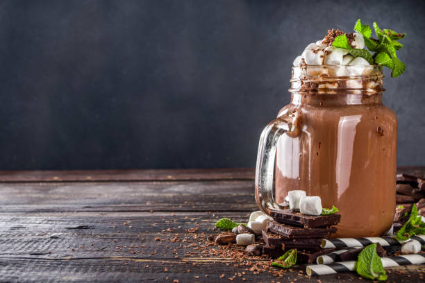 Chocolate milk shake Chocolate milk shake with sauce, marshmallows and grated chocolate, decorated with mint. On old rustic wooden table with a lot of chocolate pieces, cocoa beans and chocolate shavings chocolate shake stock pictures, royalty-free photos & images