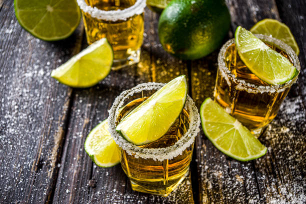 Golden tequila shots Golden tequila shots. Three tequila shot glasses with salt and lime slices, on wooden background copy space tequila shot stock pictures, royalty-free photos & images