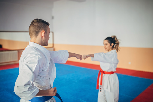 One young woman and one young man, karate students, training karate together indoors.