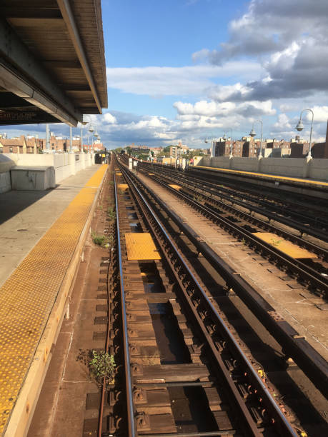 istock Looking down the overground subway tracks at an empty subway platform in Queens, NY. Empty subway platform.  Blue sky with clouds. Outdoor subway station stop in New York City. 1251512647