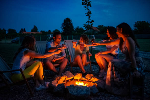 friends enjoying evening drinks by firepit outdoors. - friendly fire imagens e fotografias de stock