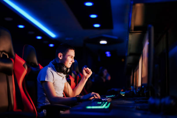istock Cheerful young gamer gesturing while playing online video game at cybercafe, portrait, side view. 1251514280