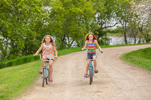 Two Girls Riding Vintage Bikes On Rural Driveway