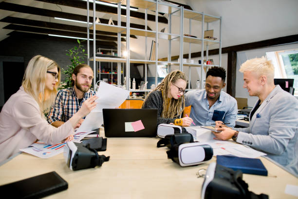 istock Business meeting. Creative team of young multiethnic colleagues, students, IT developers brainstorming while sitting at the office table together and working with laptop, tablet and papers 1251518060