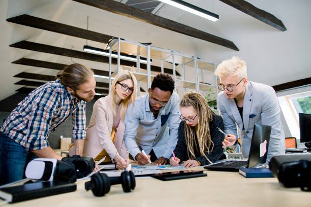 istock Creative multiethnic team of five skilled young colleagues working with data and marketing charts in modern office, leaning on the table. Full concentration at work. 1251518743